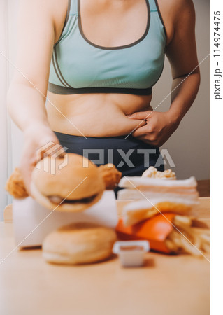 To eat or not. Cheerless plump woman looking at the burger while thinking to eat it or not 114974476