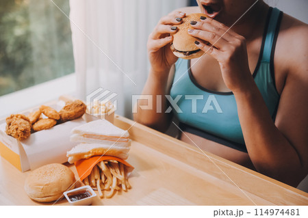 Binge eating disorder concept with woman eating fast food burger, fired chicken , donuts and desserts Binge eating disorder concept with woman eating fast food burger, fired chicken , donuts and desserts 114974481