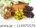 Cutting board with bunch of organic green, pink and blue grapes on white wooden background.. 114975570
