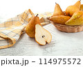 Whole and halves of pears, wicker basket and yellow kitchen towel on white wooden background.. 114975572