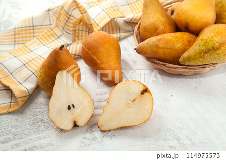 Whole and halves of pears, wicker basket and yellow kitchen towel on white wooden background.. 114975573