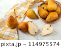 Whole and halves of pears, wicker basket and yellow kitchen towel on white wooden background.. 114975574