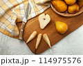 Cutting board with whole and slices pears, wicker basket and yellow kitchen towel on white wooden background.. 114975576