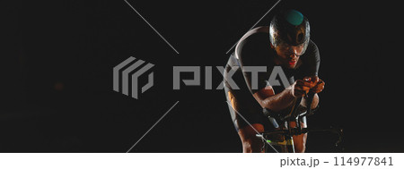 A triathlete rides his bike in the darkness of night, pushing himself to prepare for a marathon. The contrast between the darkness and the light of his bike creates a sense of drama and highlights the 114977841