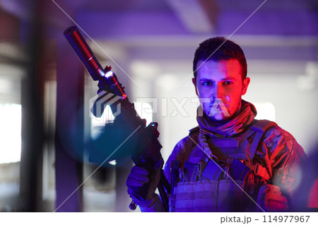 A professional soldier undertakes a perilous mission in an abandoned building illuminated by neon blue and purple lights A professional soldier undertakes a perilous mission in an abandoned building illuminated by neon blue and purple lights 114977967