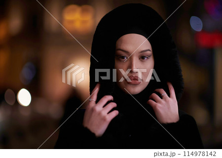 Muslim woman walking on an urban city street on a cold winter night wearing hijab Muslim woman walking on an urban city street on a cold winter night wearing hijab 114978142