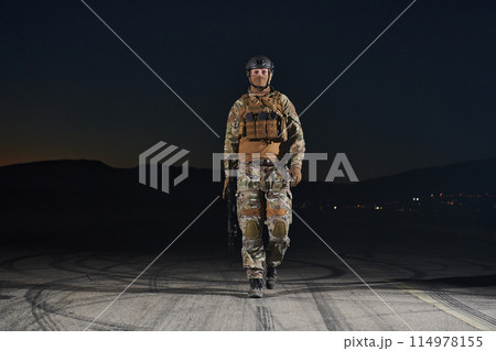 A professional soldier in full military gear striding through the dark night as he embarks on a perilous military mission 114978155