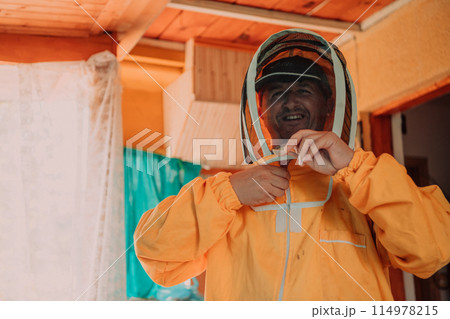 Beekeeper put on a protective beekeeping suit and preparing to enter the apiary Beekeeper put on a protective beekeeping suit and preparing to enter the apiary 114978215