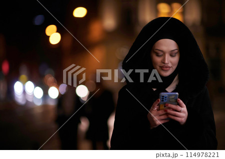 Muslim woman walking on an urban city street on a cold winter night wearing hijab Muslim woman walking on an urban city street on a cold winter night wearing hijab 114978221