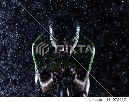 A triathlete braving the rain as he cycles through the night, preparing himself for the upcoming marathon. The blurred raindrops in the foreground and the dark, moody atmosphere in the background add 114978427