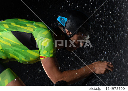 A triathlete braving the rain as he cycles through the night, preparing himself for the upcoming marathon. The blurred raindrops in the foreground and the dark, moody atmosphere in the background add A triathlete braving the rain as he cycles through the night, preparing himself for the upcoming marathon. The blurred raindrops in the foreground and the dark, moody atmosphere in the background add 114978500