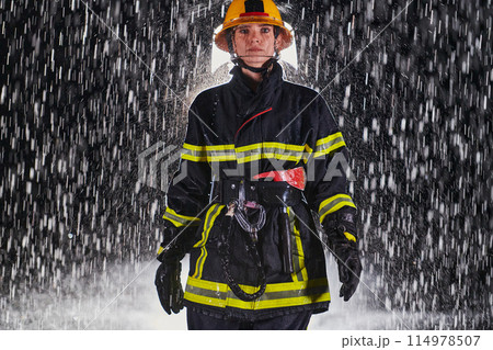 A determined female firefighter in a professional uniform striding through the dangerous, rainy night on a daring rescue mission, showcasing her unwavering bravery and commitment to saving lives. 114978507