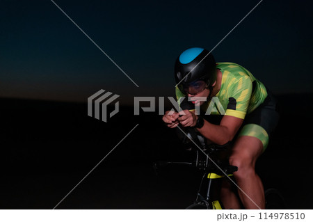 A triathlete rides his bike in the darkness of night, pushing himself to prepare for a marathon. The contrast between the darkness and the light of his bike creates a sense of drama and highlights the 114978510