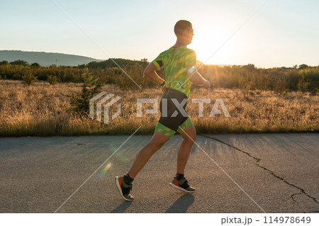 Triathlete in professional gear running early in the morning, preparing for a marathon, dedication to sport and readiness to take on the challenges of a marathon. Triathlete in professional gear running early in the morning, preparing for a marathon, dedication to sport and readiness to take on the challenges of a marathon. 114978649
