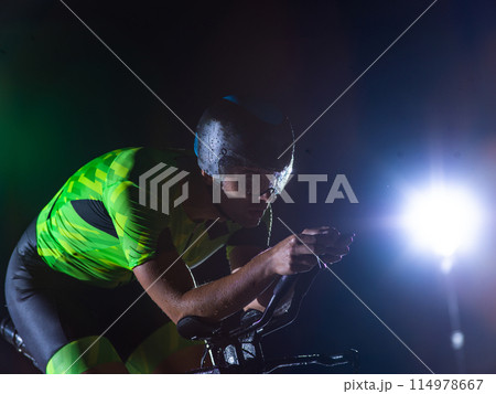 A triathlete rides his bike in the darkness of night, pushing himself to prepare for a marathon. The contrast between the darkness and the light of his bike creates a sense of drama and highlights the 114978667