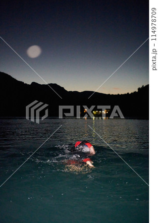 A determined professional triathlete undergoes rigorous night time training in cold waters, showcasing dedication and resilience in preparation for an upcoming triathlon swim competition 114978709