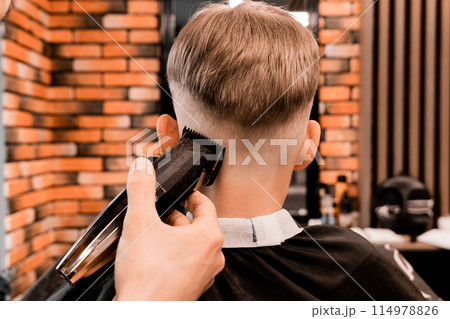 Nice european little boy getting hairstyle in barbershop. Hairdresser makes a hairstyle for a boy. 114978826