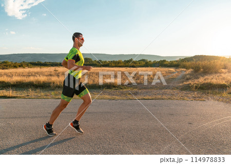 Triathlete in professional gear running early in the morning, preparing for a marathon, dedication to sport and readiness to take on the challenges of a marathon.  114978833