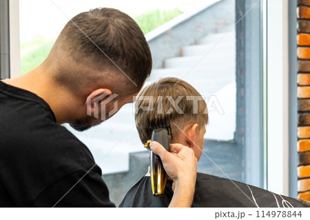 A child with very beautiful blond hair is in a barbershop and is being milled with a special hair milling machine. 114978844