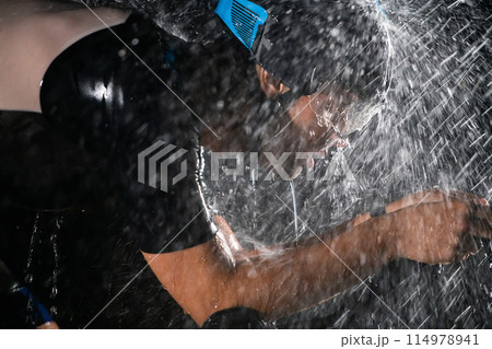 A triathlete braving the rain as he cycles through the night, preparing himself for the upcoming marathon. The blurred raindrops in the foreground and the dark, moody atmosphere in the background add 114978941
