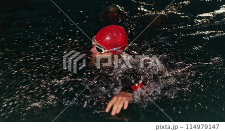 A determined professional triathlete undergoes rigorous night time training in cold waters, showcasing dedication and resilience in preparation for an upcoming triathlon swim competition A determined professional triathlete undergoes rigorous night time training in cold waters, showcasing dedication and resilience in preparation for an upcoming triathlon swim competition 114979147