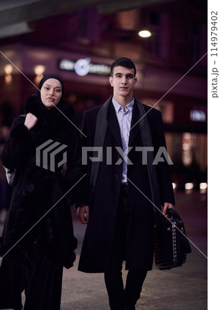 Happy multicultural business couple walking together outdoors in an urban city street at night near a jewelry shopping store window. 114979402