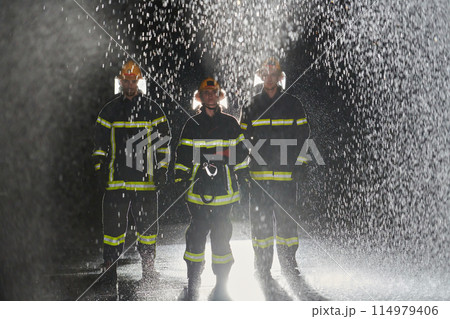A group of professional firefighters marching through the rainy night on a rescue mission, their determined strides and fearless expressions reflecting their unwavering bravery and unwavering 114979406
