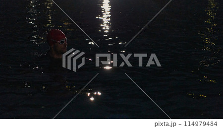 A determined professional triathlete undergoes rigorous night time training in cold waters, showcasing dedication and resilience in preparation for an upcoming triathlon swim competition A determined professional triathlete undergoes rigorous night time training in cold waters, showcasing dedication and resilience in preparation for an upcoming triathlon swim competition 114979484