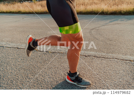 Closeup of muscular legs of a triathlete in professional equipment running early in the morning, preparing for a marathon, dedication to sports and readiness for marathon challenges 114979682