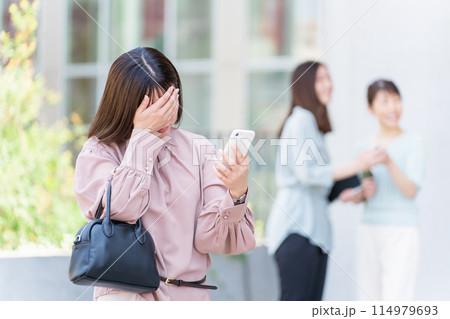 オフィスビルの前でスマホを操作しながら困る・悩む若いアジア人ビジネスウーマン（失敗・トラブル） 114979693