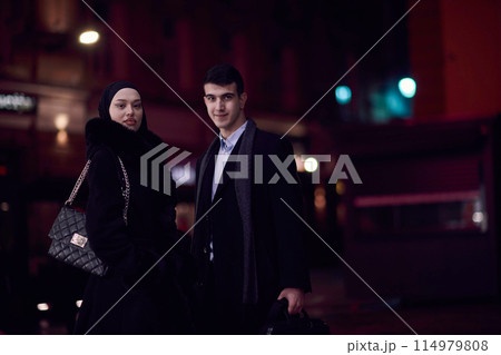 Happy multicultural business couple walking together outdoors in an urban city street at night near a jewelry shopping store window. 114979808