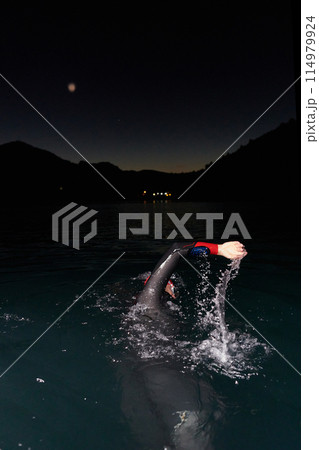 A determined professional triathlete undergoes rigorous night time training in cold waters, showcasing dedication and resilience in preparation for an upcoming triathlon swim competition 114979924
