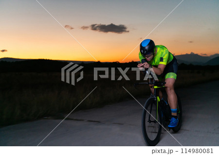 A triathlete rides his bike in the darkness of night, pushing himself to prepare for a marathon. The contrast between the darkness and the light of his bike creates a sense of drama and highlights the 114980081