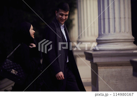 Happy multicultural business couple walking together outdoors in an urban city street at night near a jewelry shopping store window. 114980167