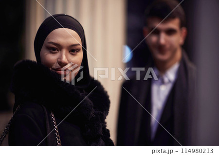Happy multicultural business couple walking together outdoors in an urban city street at night near a jewelry shopping store window. Happy multicultural business couple walking together outdoors in an urban city street at night near a jewelry shopping store window. 114980213
