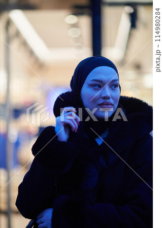 Muslim woman walking on an urban city street on a cold winter night wearing hijab 114980284