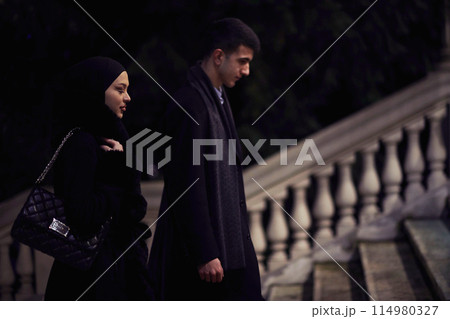 Happy multicultural business couple walking together outdoors in an urban city street at night near a jewelry shopping store window. 114980327