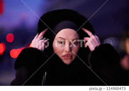 Muslim woman walking on an urban city street on a cold winter night wearing hijab 114980473
