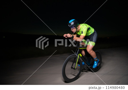 A triathlete rides his bike in the darkness of night, pushing himself to prepare for a marathon. The contrast between the darkness and the light of his bike creates a sense of drama and highlights the A triathlete rides his bike in the darkness of night, pushing himself to prepare for a marathon. The contrast between the darkness and the light of his bike creates a sense of drama and highlights the 114980480