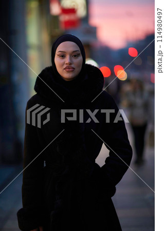 Muslim woman walking on an urban city street on a cold winter night wearing hijab 114980497