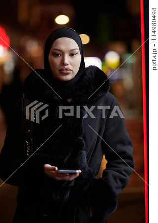 Muslim woman walking on an urban city street on a cold winter night wearing hijab 114980498