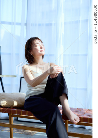 部屋の中で椅子に座って朝日を浴びる女性 114980630