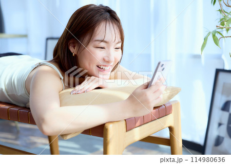 部屋の中で椅子に寝そべってスマホを見る女性 部屋の中で椅子に寝そべってスマホを見る女性 114980636