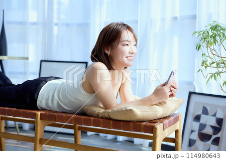 部屋の中で椅子に寝そべってスマホを見る女性 部屋の中で椅子に寝そべってスマホを見る女性 114980643