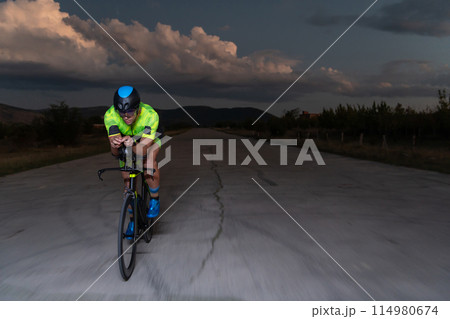 A triathlete rides his bike in the darkness of night, pushing himself to prepare for a marathon. The contrast between the darkness and the light of his bike creates a sense of drama and highlights the A triathlete rides his bike in the darkness of night, pushing himself to prepare for a marathon. The contrast between the darkness and the light of his bike creates a sense of drama and highlights the 114980674