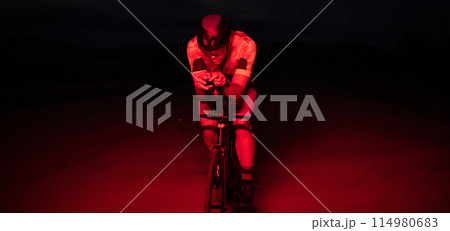 A triathlete rides his bike in the darkness of night, pushing himself to prepare for a marathon. The contrast between the darkness and the light of his bike creates a sense of drama and highlights the A triathlete rides his bike in the darkness of night, pushing himself to prepare for a marathon. The contrast between the darkness and the light of his bike creates a sense of drama and highlights the 114980683