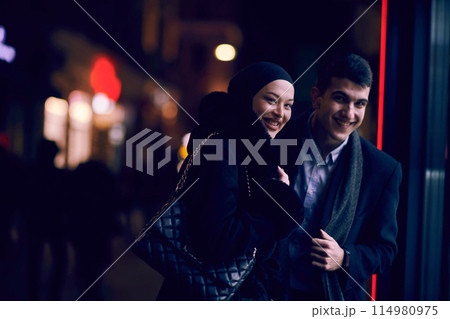 Happy multicultural business couple walking together outdoors in an urban city street at night near a jewelry shopping store window. 114980975