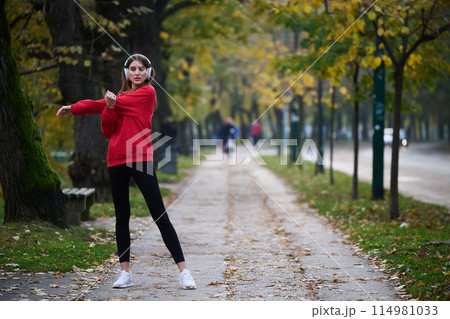 Young beautiful woman running in autumn park and listening to music with headphones on smartphone Young beautiful woman running in autumn park and listening to music with headphones on smartphone 114981033