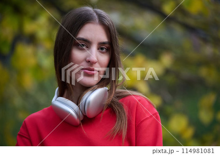 Portrait of running woman after jogging in the park on autumn seasson. Female fitness model training outside on a cozy fall day and listening to music over smartphone. Portrait of running woman after jogging in the park on autumn seasson. Female fitness model training outside on a cozy fall day and listening to music over smartphone. 114981081