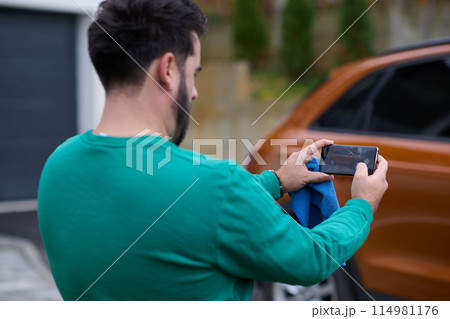 man taking photos on a smartphone of a car preparing for sale  114981176